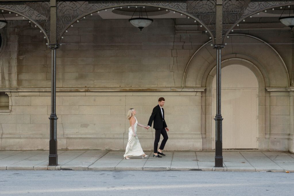 Elegant couple walks under curved arch ways at the Milwaukee City Hall.