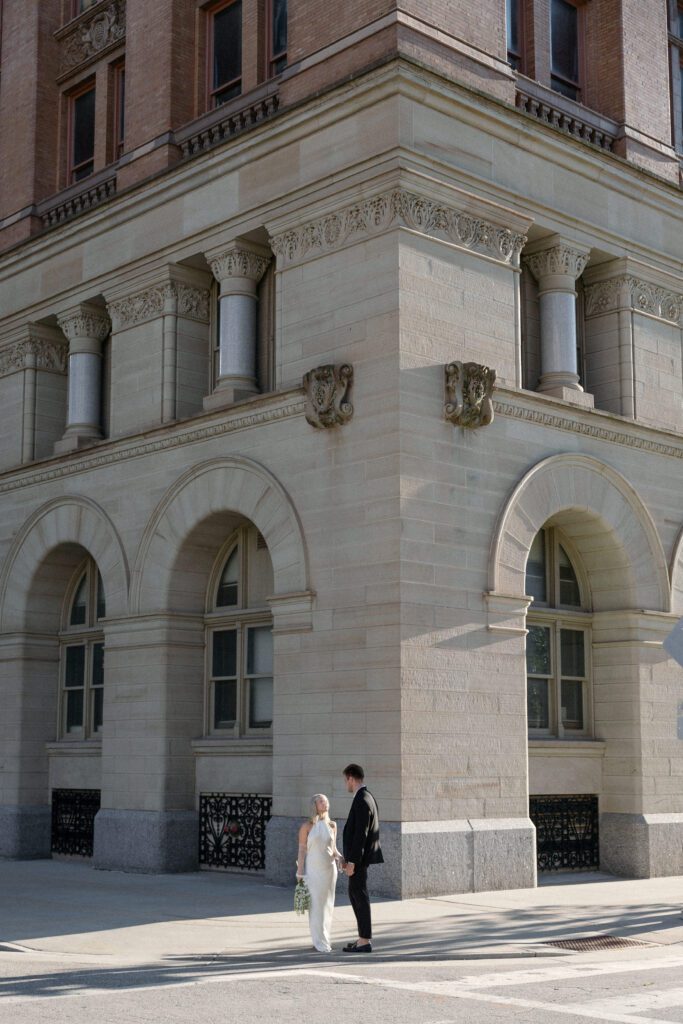 Couple walks hand in hand outside Milwaukee City Hall after their elopement.