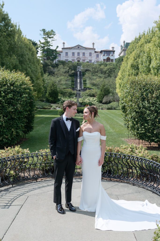 Wide shot of the bride and groom holding hands on their wedding day with the view of The Villa Terrace in the background.