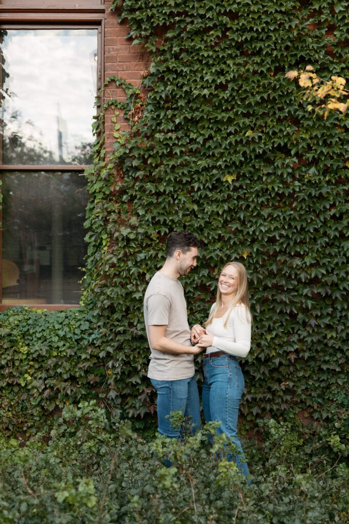 Couple laughs by an ivy wall near the Memorial Union during their engagement session.