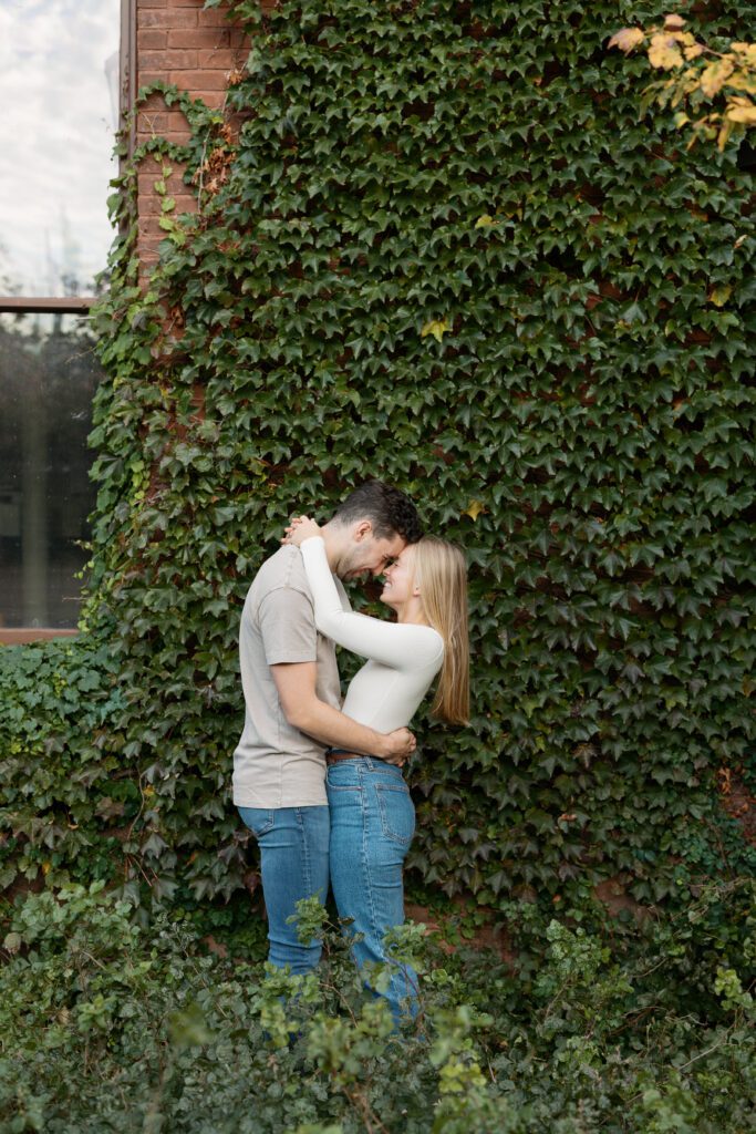 Couple hugs and smiles near an ivy wall near the Memorial Union.