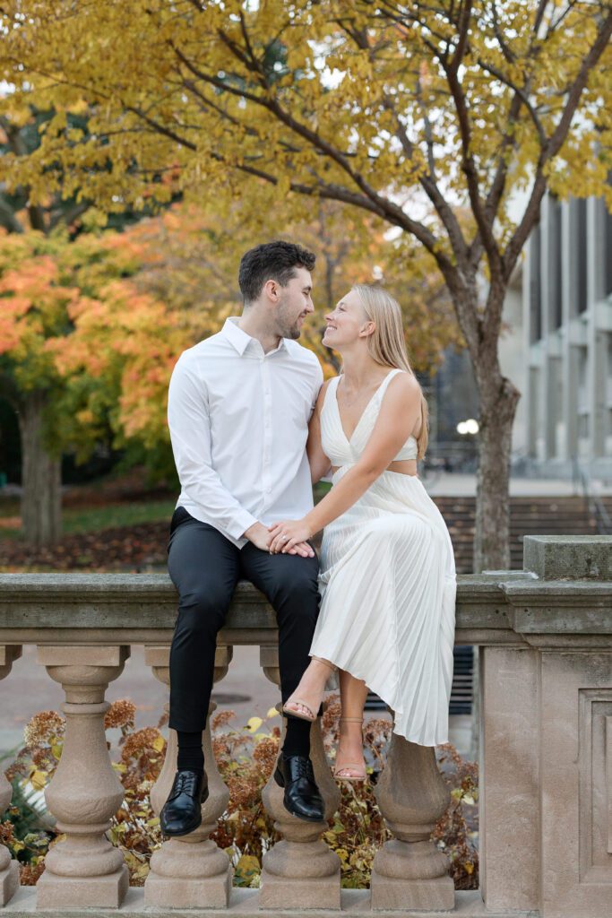 Couple sitting on edge looking into each other's eyes at their engagement session.