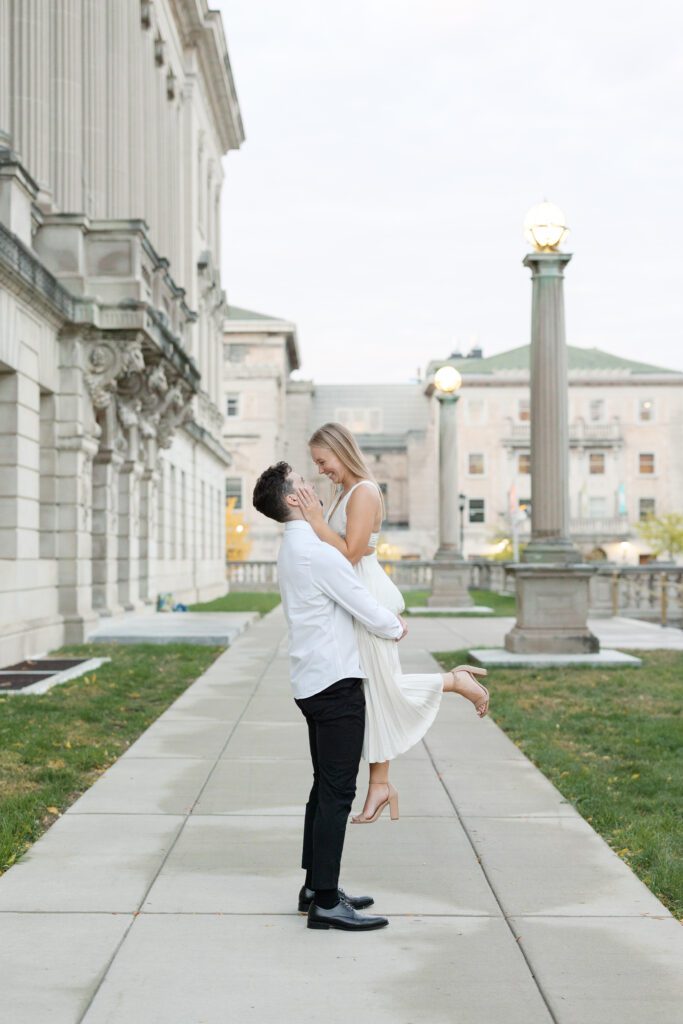 Couple wrapped in each other's arms with the Memorial Union visible behind them.