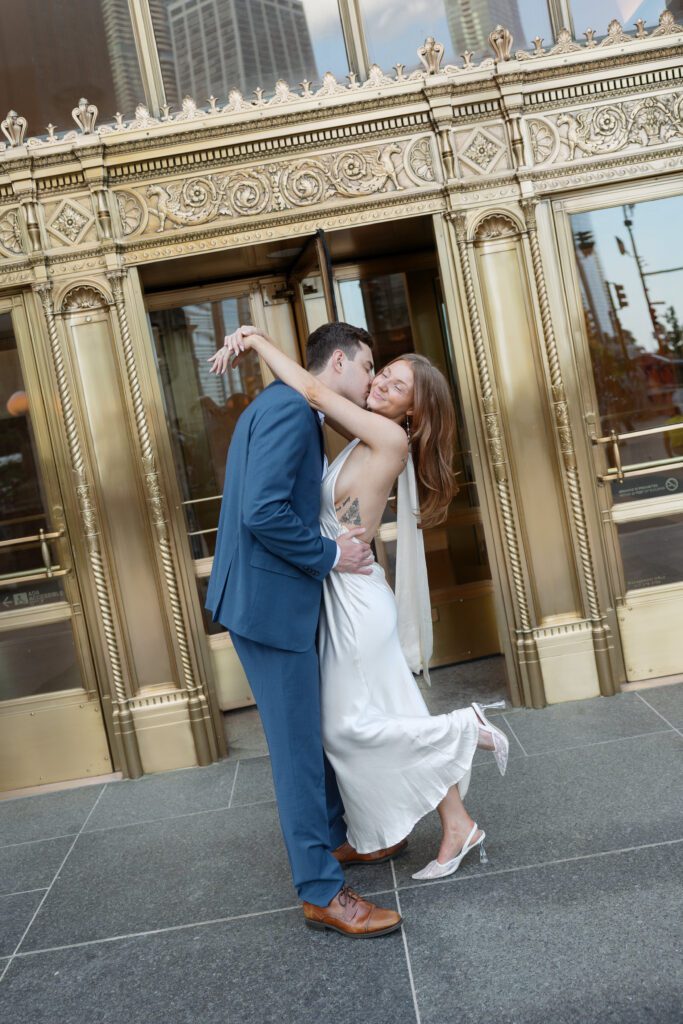 Couple dip kissing in front of the gold Wrigley Building in downtown Chicago.