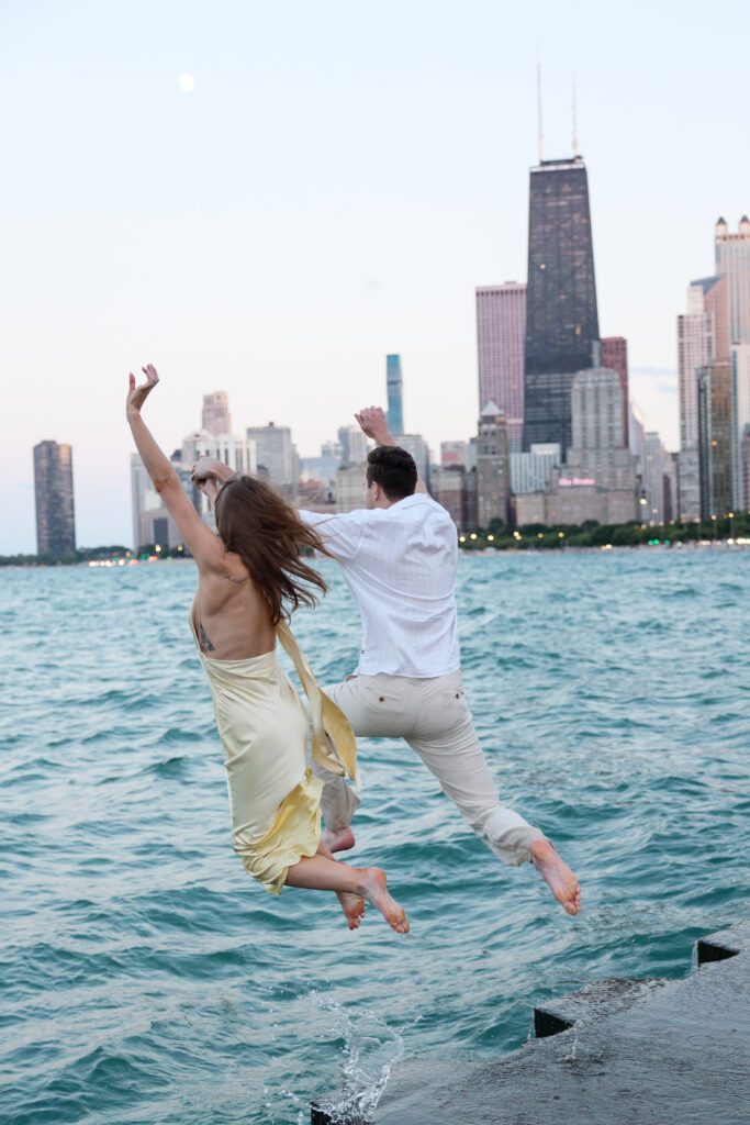 Couple jumping into the blue water of Lake Michigan during their North Avenue Beach engagement session.