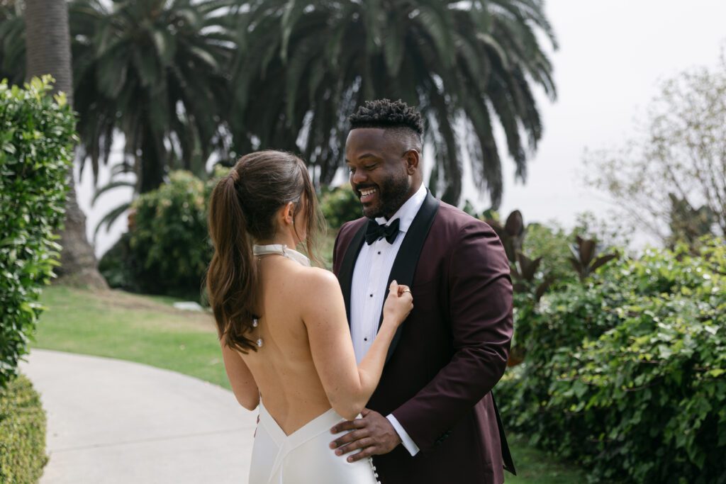 Bride and groom embracing with palm trees and ocean waves in the background at their Bel Air Bay Club wedding.