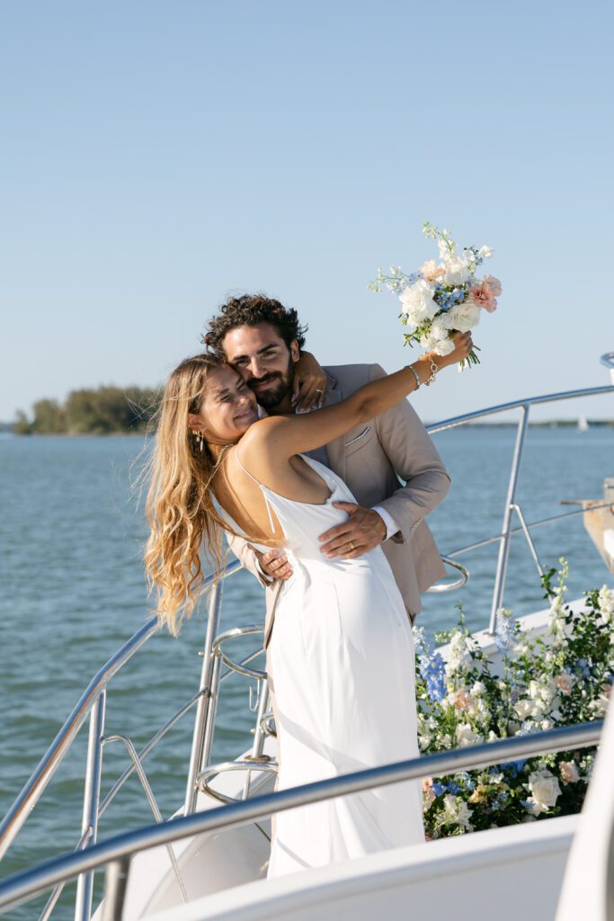 The couple cuddles closely on the yacht, wrapped in each other's arms, with the vibrant sunset creating a romantic backdrop for their West Palm Beach Boat Elopement.