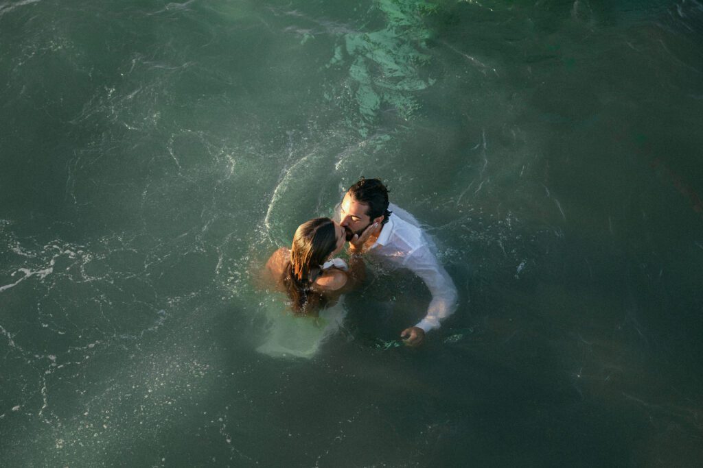 The couple in the water sharing a kiss, surrounded by the beauty of the ocean, capturing a romantic moment from their West Palm Beach Boat Elopement.