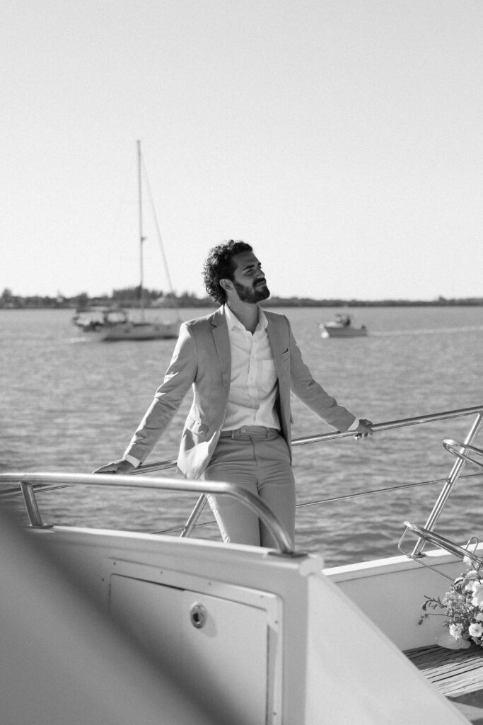 A thoughtful portrait of the groom gazing lovingly at his bride on the stern of the boat during their West Palm Beach Boat Elopement.